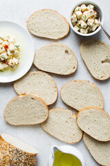 Top view of marinated feta cheese cubes and slices of toasted bread on a white plate. Cheese cubes in a ramekin with bread, flat lay of feta cheese cubes and slices of toast
