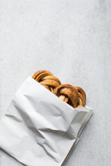 top view of Swedish cinnamon buns in a white bakery bag, cinnamon twists in a white paper bag, top...