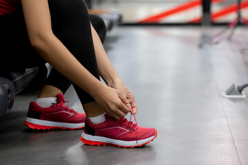 Closeup young woman tying shoelace with hands for jogging in fitness gym sport club, female preparing workout and exercise with wearing sportswear and sneaker, healthcare and motivation.