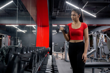 Obraz na płótnie Canvas Young asian woman in sportswear workout with lifting dumbbell for exercise in fitness gym training sport club, female practice and endurance with working out, sport and healthcare, one person.