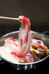 Hand holding bamboo chopsticks a piece of belly pork sliced for delicious Sukiyaki. Japanese hot pot also known as Shabu Shabu or Sukiyaki is a Japanese style.