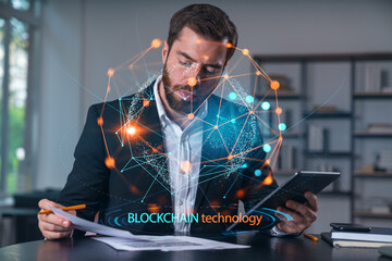 Considered businessman in formal wear signing contract holding tablet device at office room with papers. Concept of successful business deal, agreement, partnership, documents. BLockchain icons.