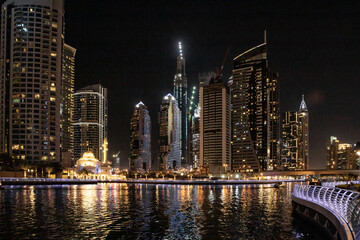 Fototapeta na wymiar Night view from the promenade of Dubai Marina with illuminated skyscrapers, a water channel, yachts and ships in Dubai city, United Arab Emirates