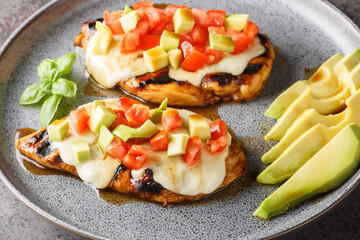 Grilled chicken breast marinated with balsamic vinegar and honey topped with cheese, avocado and tomatoes close-up in a plate on the table. horizontal