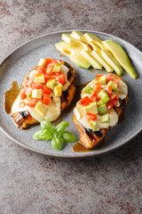 Grilled chicken breast topped with melted cheese, sliced avocado and tomatoes close-up in a plate on the table. Vertical
