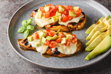 Grilled California Avocado Chicken marinates in balsamic vinaigrette topped with fresh mozzarella, avocado, and tomato closeup on the plate on the table. Horizontal