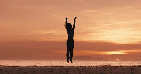 Back view woman winner at sunset jumping on golden sunset background showing yes gesture. Concept of winning. Happy woman jumping with raised hand, celebrating life achievements, looking at sea sunset