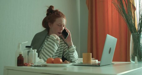 pale week red-haired unwell businesswoman coughing, calling ambulance while sitting at desk and working with laptop at home in the living room, slow motion online consultation