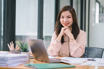 Fototapeta na wymiar A portrait of a smiling, young, beautiful, professional, and confident millennial Asian businesswoman using a digital tablet to analyze sales data at a modern office.