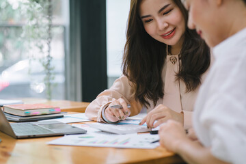 Two businesspeople or an accountant team are analyzing data charts, graphs, and a dashboard on a laptop screen in order to prepare a statistical report and discuss financial data in an office.