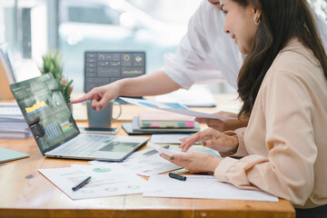 Two businesspeople or an accountant team are analyzing data charts, graphs, and a dashboard on a laptop screen in order to prepare a statistical report and discuss financial data in an office.