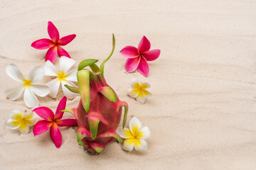 Obraz na płótnie Canvas Dragon fruit with plumeria flowers on sand beach on summer for your holiday background design.