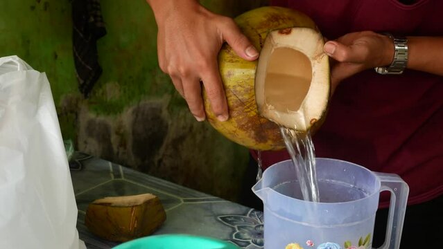 the young coconut seller is pouring coconut water into the container