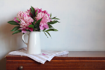 A bouquet of pink peonies on a table against a white wall.