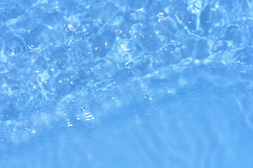 Obraz premium Blue water with ripples on the surface. Defocus blurred transparent blue colored clear calm water surface texture with splashes and bubbles. Water waves with shining pattern texture background.