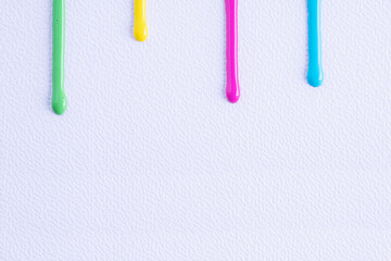 Green, Yellow, Pink and Blue drops of paint flow down on white canvas. Abstract art. Colorful paint...