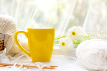 Coffee morning.  Yellow steaming cup of hot coffee for relax after working hobbies crochet on white wooden near window with flowers