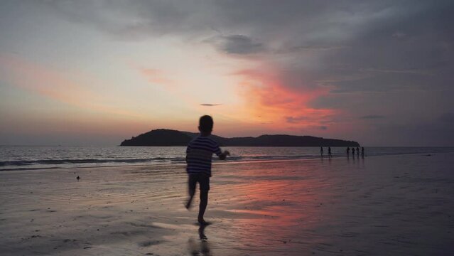 Little boy is running along a sand beach at sunset