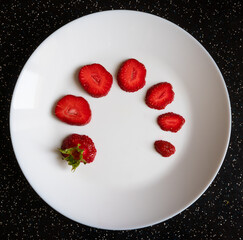 Sliced ripe strawberries on a white plate on the table, top view