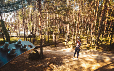 Palanga, Lithuania - 2023: young woman girl sliding along zipline in fir tree forest in summer. Lithuania adventure park in HBH. © Evaldas