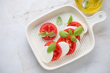 Beige serving tray with italian traditional caprese, horizontal shot on a light-beige marble background, high angle view