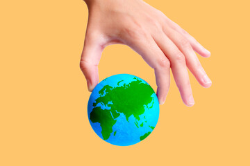 Hand Pinch-Holding a Green and Blue Globe on Yellow