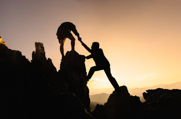 Concept of business, Hikers climbing up mountain cliff and one of them giving helping hand. People...