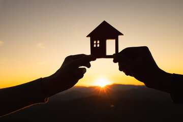 silhouette of male and female hands holding model house at sunset Concept of buying houses, real...