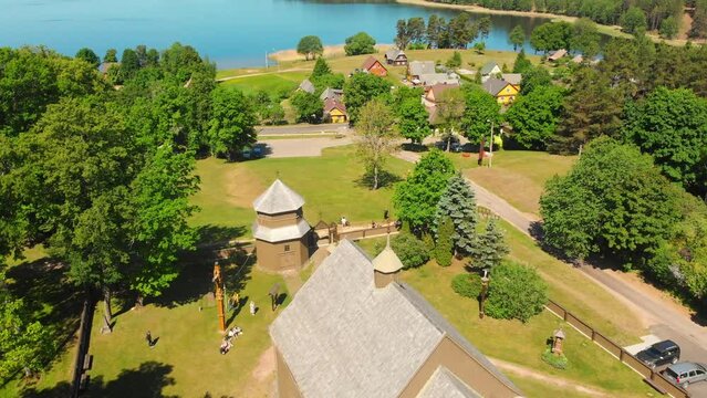 Aerial view Young lithuanians relax on sunday mass by St. Joseph Church in Paluse, Lithuania. Stave Churches in Europe. Old heritage sites. Walls formed by vertical wooden boards.