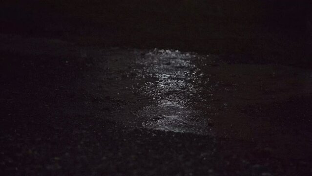Puddle of water during a rainstorm at night. Raining on the ground. Rainstorm on gravel. Heavy rain. Dark.