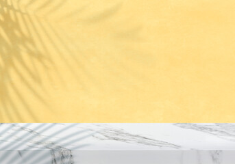 Empty white marble tabletop with leaves shadow on textured pastel yellow wall for product presentation