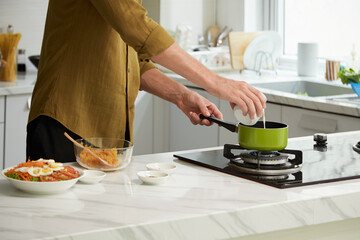 Cropped image of man adding glass of cream in saucepan