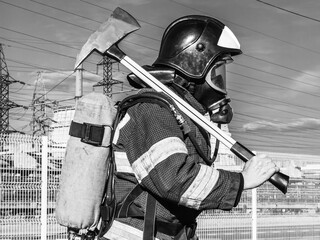 A firefighter in a helmet and breathing apparatus put an assault axe on his shoulder. A firefighter...