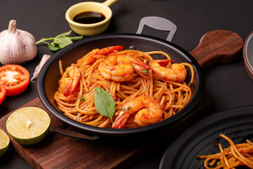 Fried Spaghetti or Fried Noodles Tomato sauce and prawns on a blue plate On a black wooden table top, top view