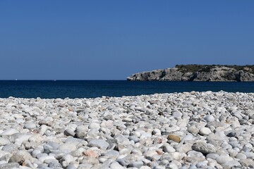 Pebble beach of the Greek island of Rhodes with blue sea and rocky mountains in the background
