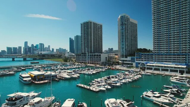 Aerial Panning Shot Of Boats Moored At Harbor Near Modern Buildings, Drone Flying Over Sea In City Against Sky On Sunny Day - Miami, Florida