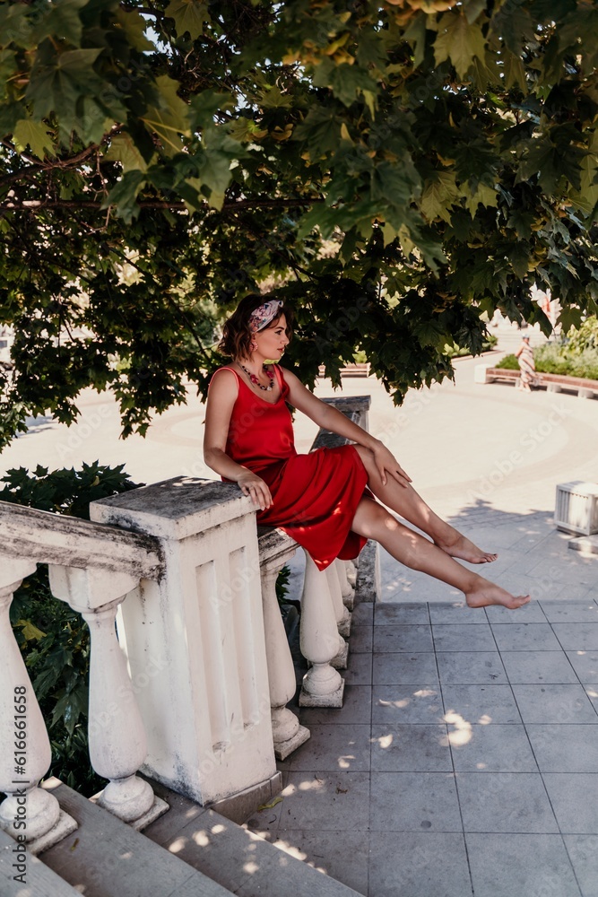 Wall mural woman in a red silk dress and a bandage on her head smiles against the background of the leaves of a