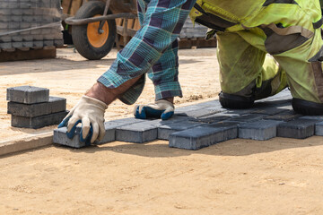 A worker laying paving stones at a sidewalk construction site, close up
Pracownik układający kostkę brukową na placu budowy chodnika, z bliska