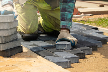 A worker laying paving stones at a sidewalk construction site, close up
Pracownik układający...