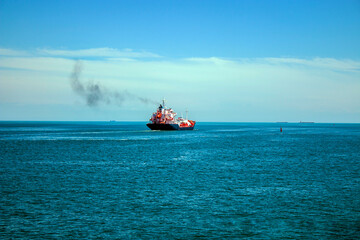 A large beautiful ship with a large number of containers floats on the horizon in the azure sea and releases smoke from the chimney