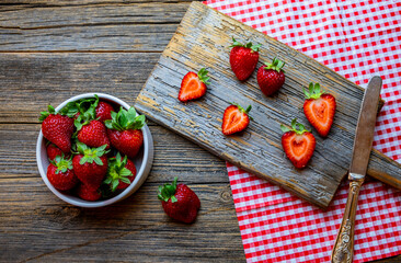 Fresh red strawberries, organic strawberries in white bowl on wooden background, chopped strawberries on a wooden cutting board, top view.