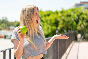 Young blonde woman with an apple at outdoors with surprise facial expression