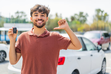 Young Arabian handsome man holding car key at outdoors proud and self-satisfied