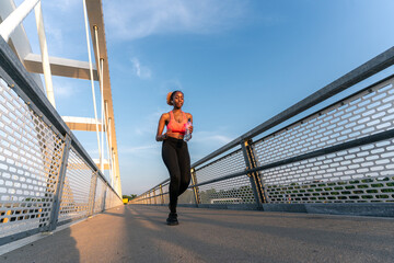 As the sun sets, she runs across the bridge, a bottle in her hand, periodically glancing at her watch.