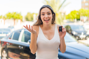 Young pretty woman holding car keys at outdoors with shocked facial expression