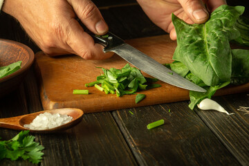 Close-up of male hands preparing salad with fresh vegetables and spinach. Cooking vegetarian food at home on the kitchen table