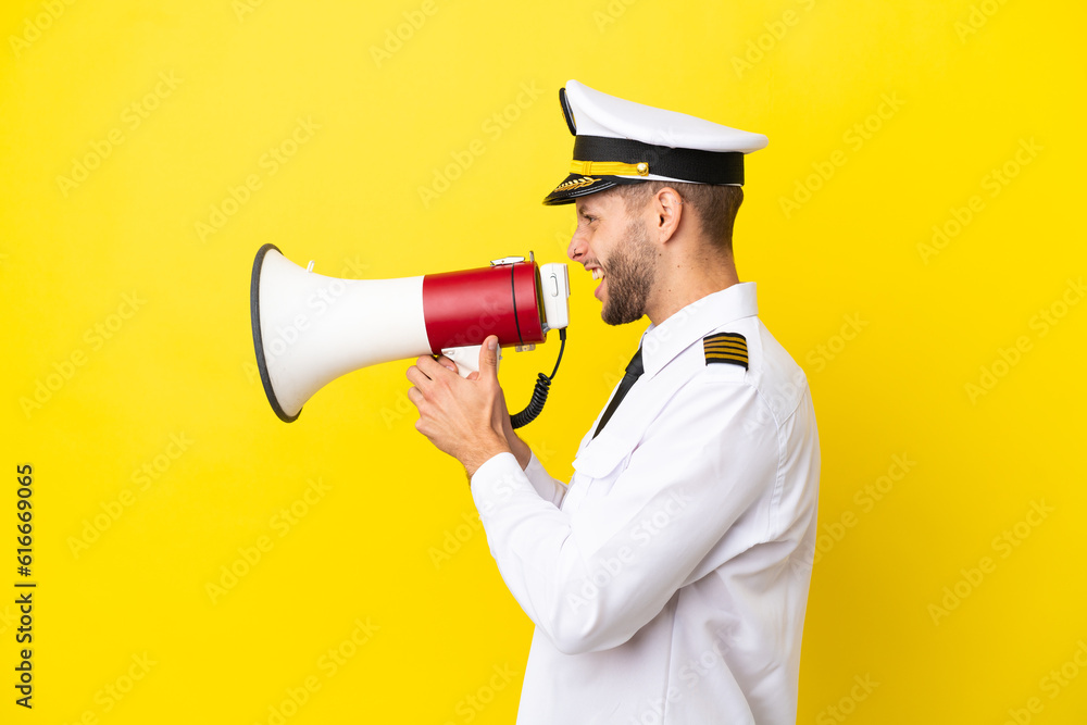 Poster Airplane caucasian pilot isolated on yellow background shouting through a megaphone