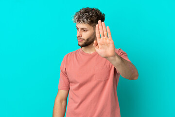Naklejka premium Young handsome caucasian man isolated on blue background making stop gesture and disappointed
