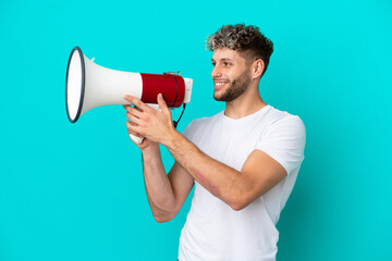 Young handsome caucasian man isolated on blue background shouting through a megaphone to announce something
