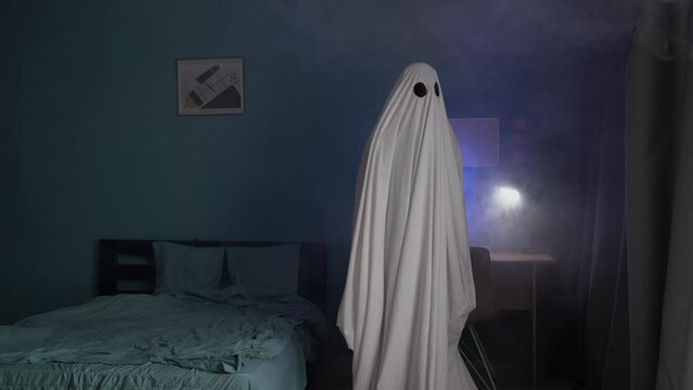 Ghostly figure in a room near the bed, Halloween scene, man covered with a white sheet in smoke